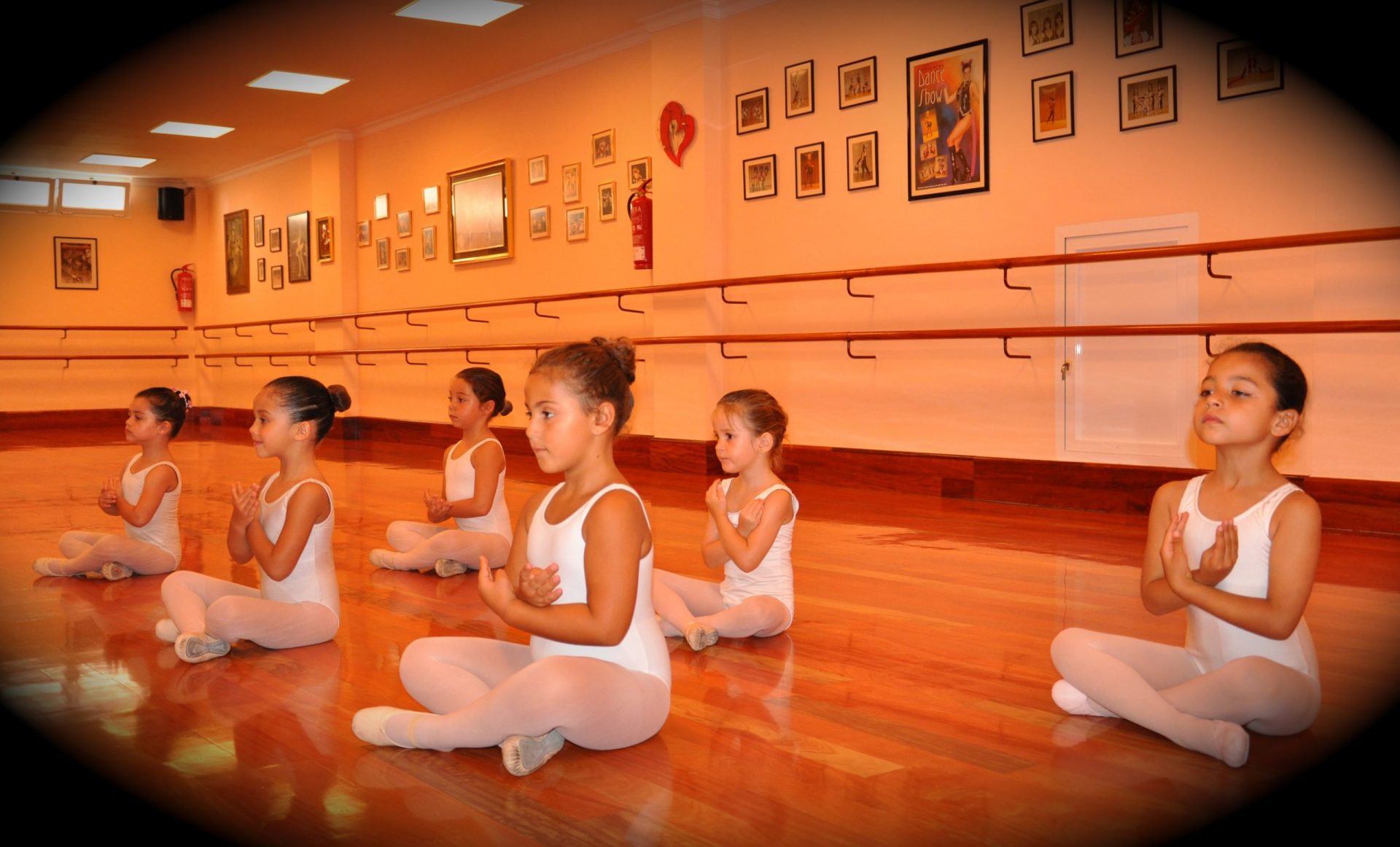 Foto de las alumnas de Predanza I del Centro de Danza Sandra Santa Cruz sentadas en el suelo perfectamente colocadas con los brazos en flor. Estas clases son para alumnoado de 3 a 5 años.