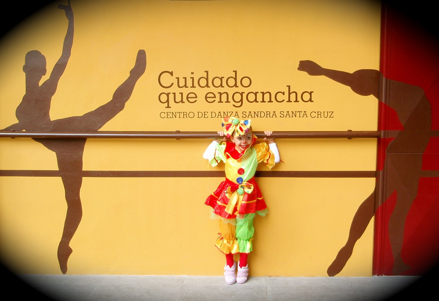Foto de una alumna de 6 años en la fachada del Centro de Danza Sandra Santa Cruz agarrada a su barra y vestida de payasete.