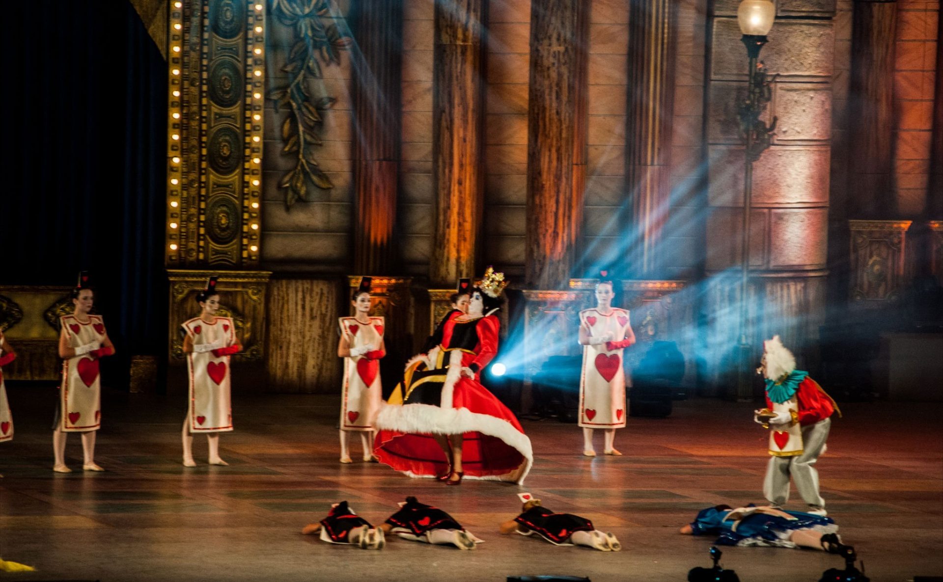 Foto "Alicia en el País de las Maravillas" del Centro de Danza Sandra Santa Cruz en el Carnaval Infantil de LPGC, donde la Reina de Corazones corre delante de un grupo de cartas alineadas mientras que Alicia y 3 cartas están tumbadas boca a bajo en el suelo.