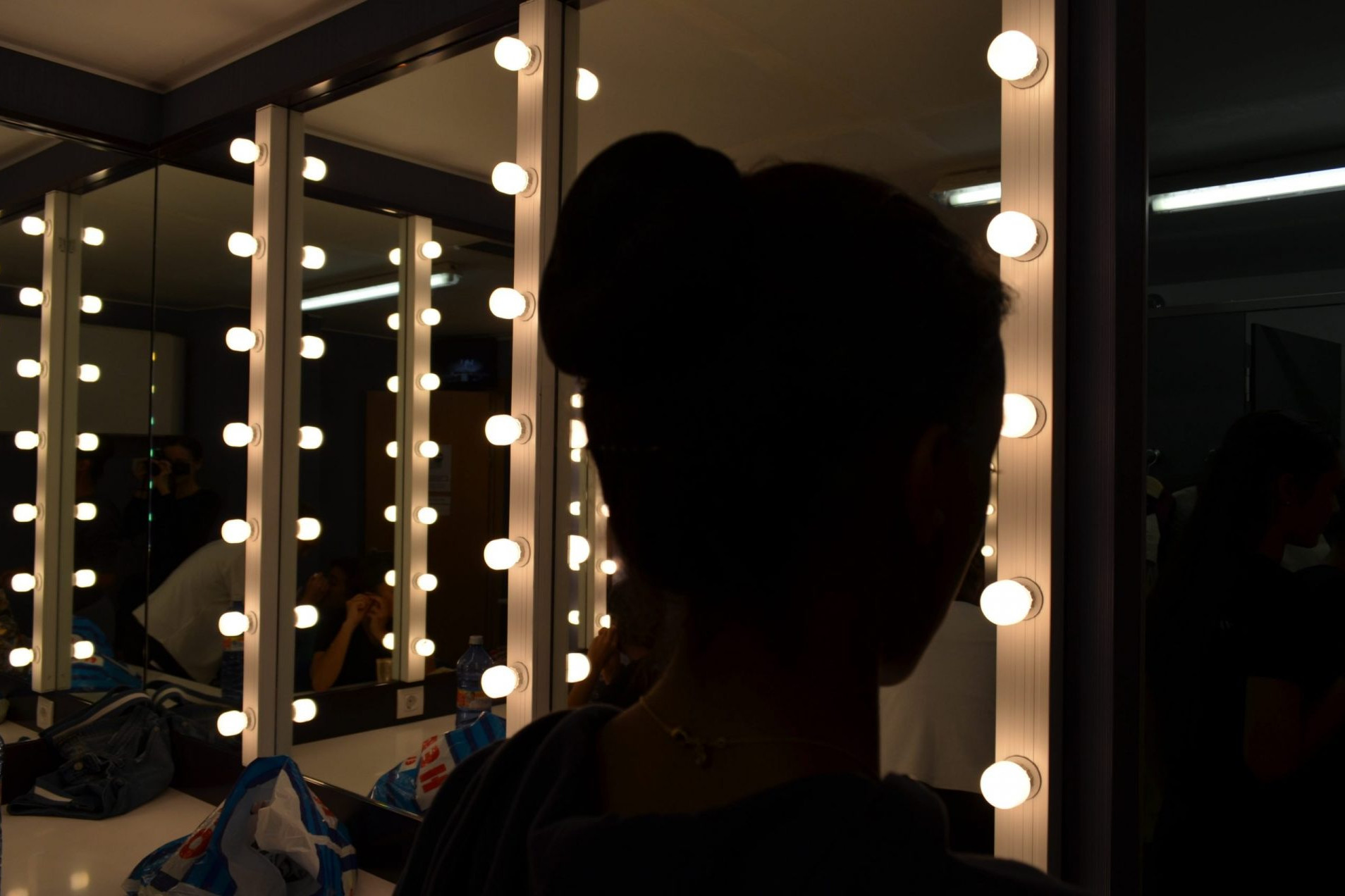 Foto de la silueta de una bailarina en camerino a contraluz de espalda al espejo