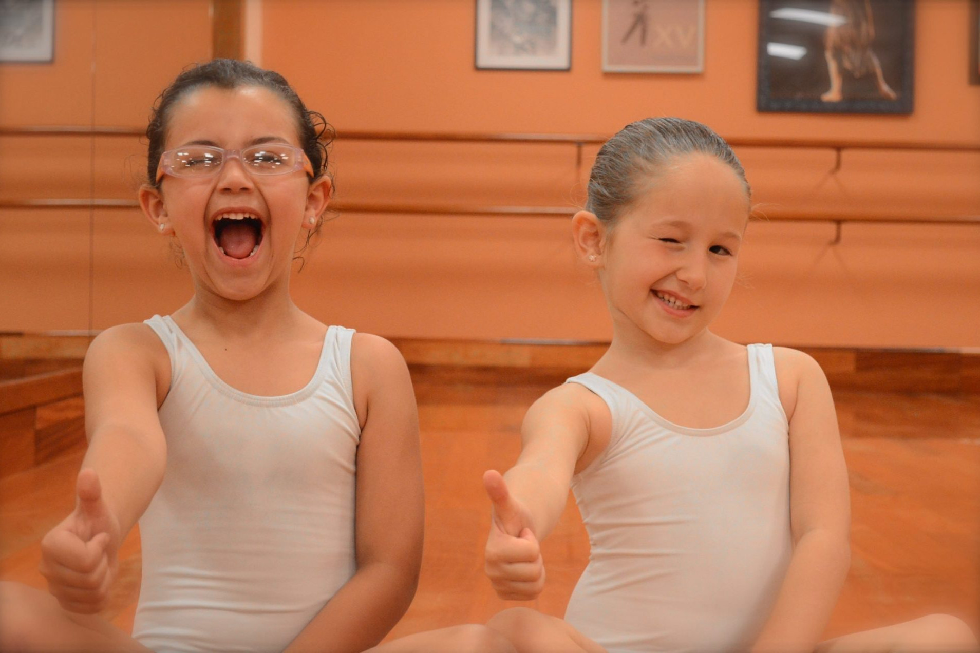 Foto de dos alumnas de 5 años del Centro de Danza Sandra Santa Cruz sentadas en la Sala de baile qguiñando un ojo y el pulgar de la mano derecha hacia arriba_DSC_0268