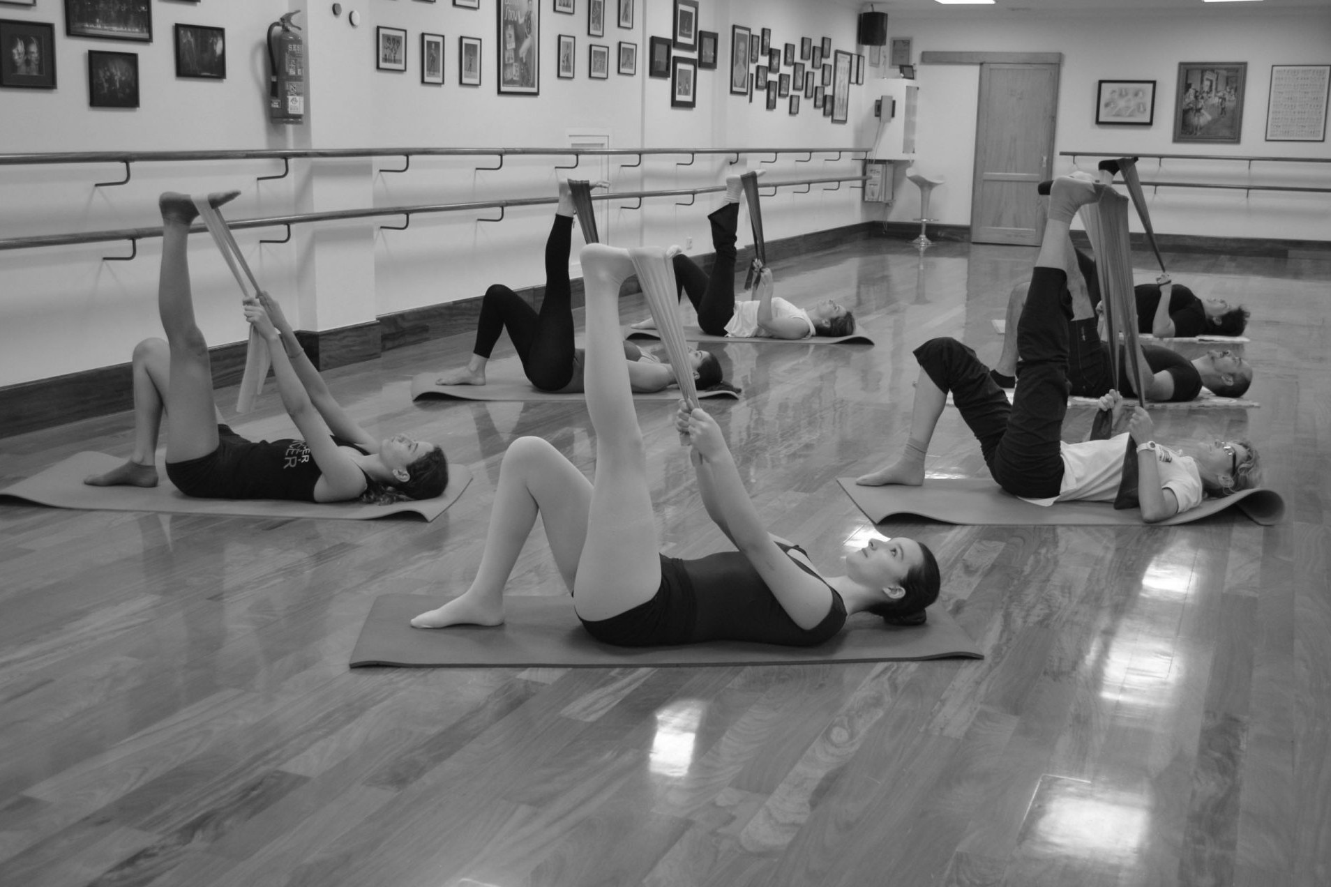 Ballet para adultos. Foto en el Centro de Danza Sandra Santa Cruz, donde un grupo de alumnos acostados en una colchoneta tienen un pie elevado que sujetan con una banda de paraband durante una clase de SLIM BALLET con fit-ball y bandas elásticas para tener mejor forma física.