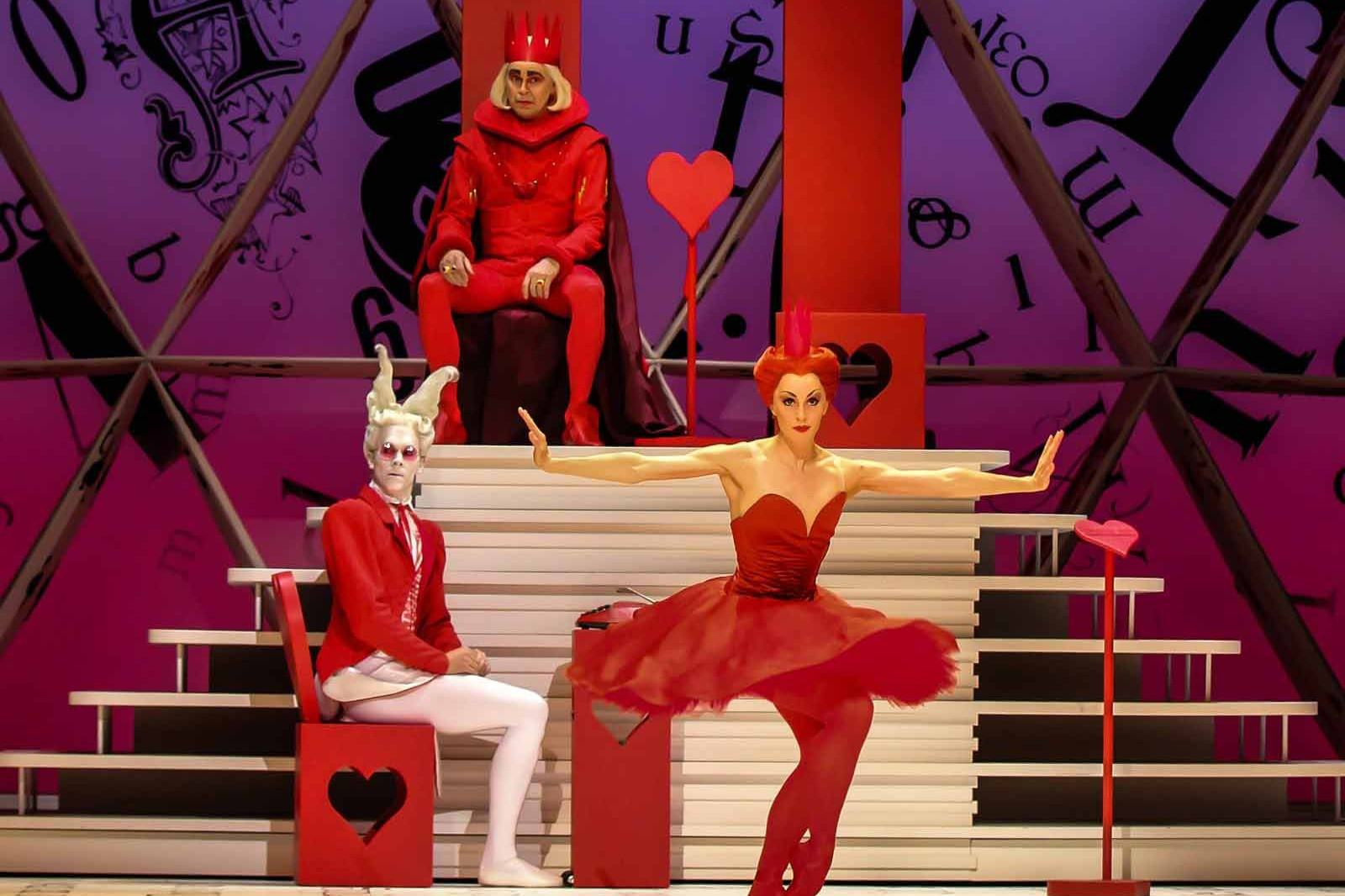Foto de Alicia en el País de las Maravillas del Royal Ballet donde se ve al rey en el fondo, el conejo a mitad de plano y la Reina de Corazones delante y como no, enfadada.