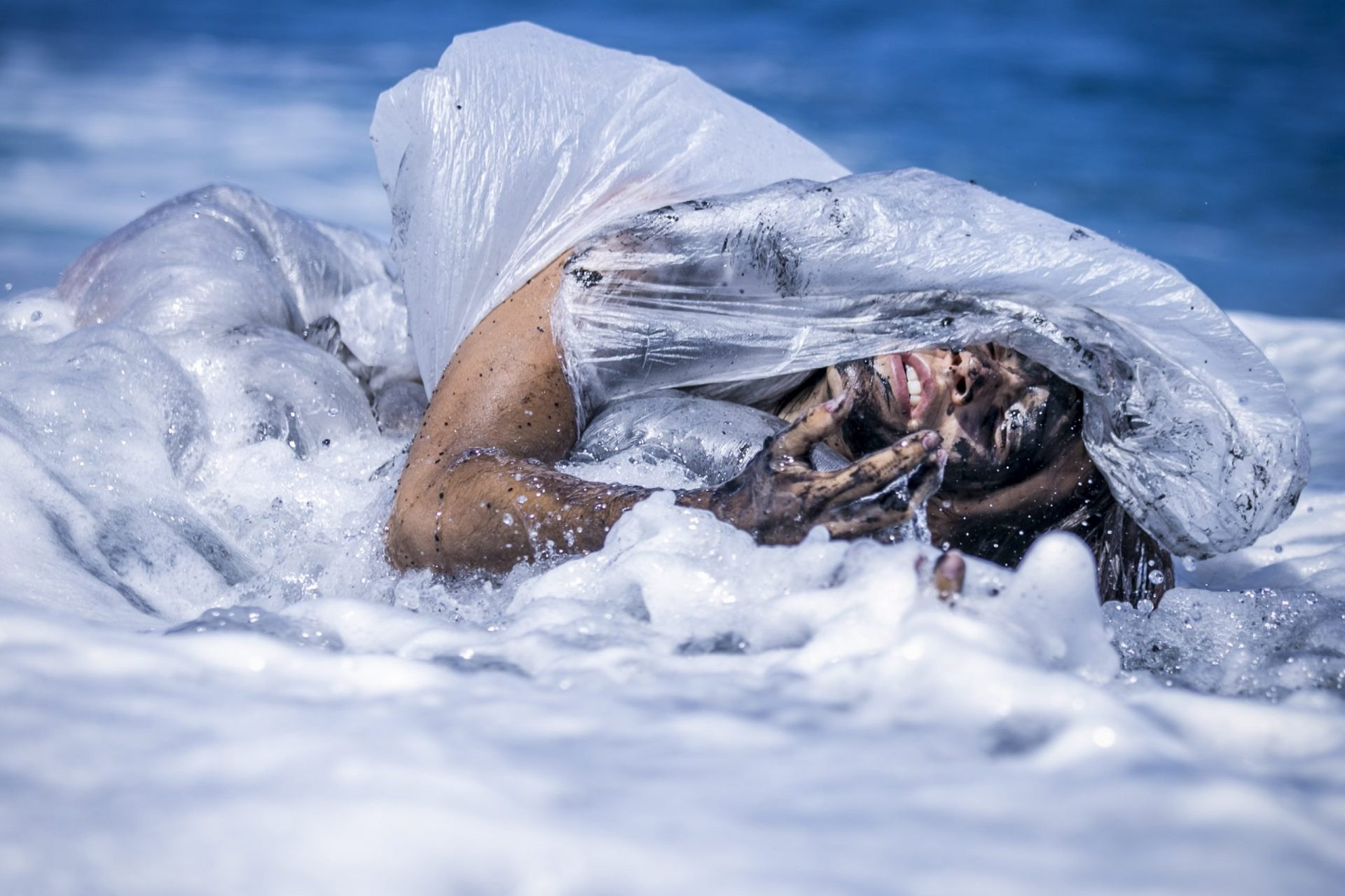 Una modelo está enredada en plástico y alquitrán mientras es vapuleada por las olas del mar. Fotografía de 