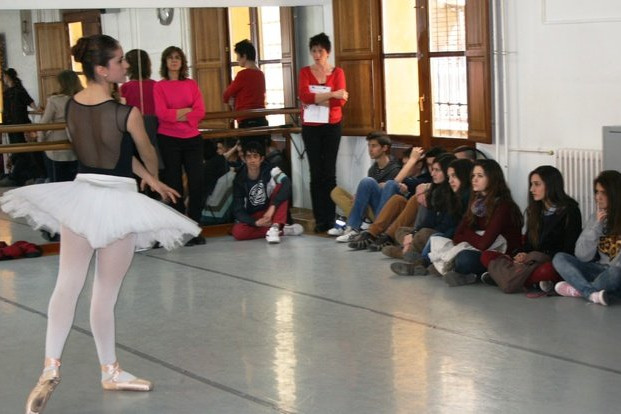 Foto de una baialrina con un tutú en una sala de baile y público sentado en el suelo. Jornada de puertas abiertas del Conservatorio de Alicante