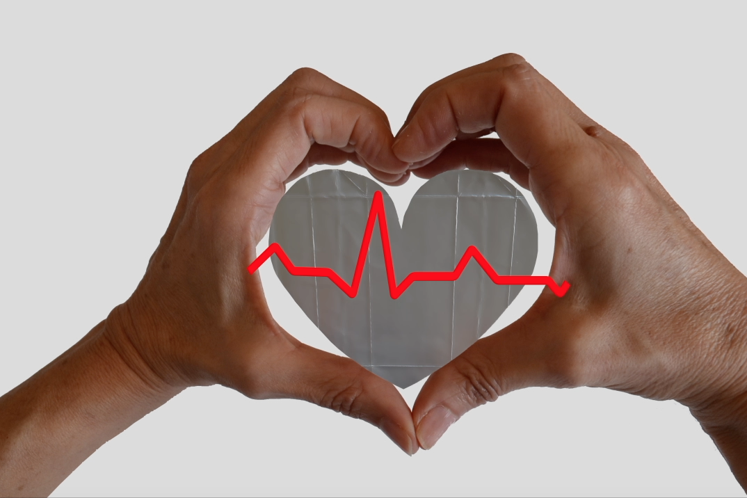 Foto de las manos de Sandra Santa Cruz abrazando a un corazón que en el centro tiene los latidos del corazón. Taller de reutilización 