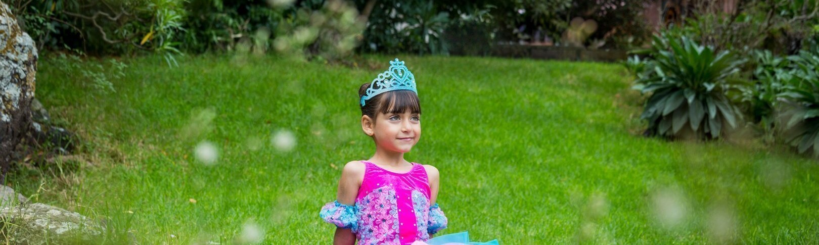 Una niña de 6 años sentada feliz en el Jardín Canario vestida con maravillosos tutú turquesa y fucsia es la foto de bienvenida al curso 20/21 del Centro de Danza Sandra Santa Cruz. Te esperamos para vivir momentos entrañables con nuestro alumnado. Fotografía: Ethel Bartrán.