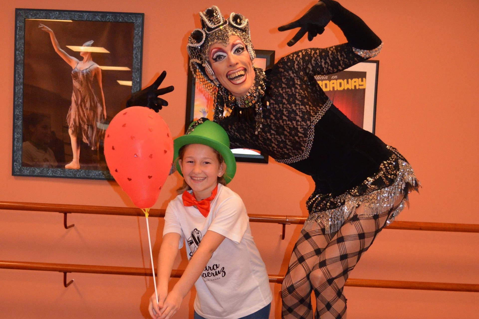 Foto de Pio Drag en el Centro de Danza Sandra Santa Cruz con una de sus alumnas que lleva puesta una pajarita roja y un bombín verde y que sujeta un globo rojo