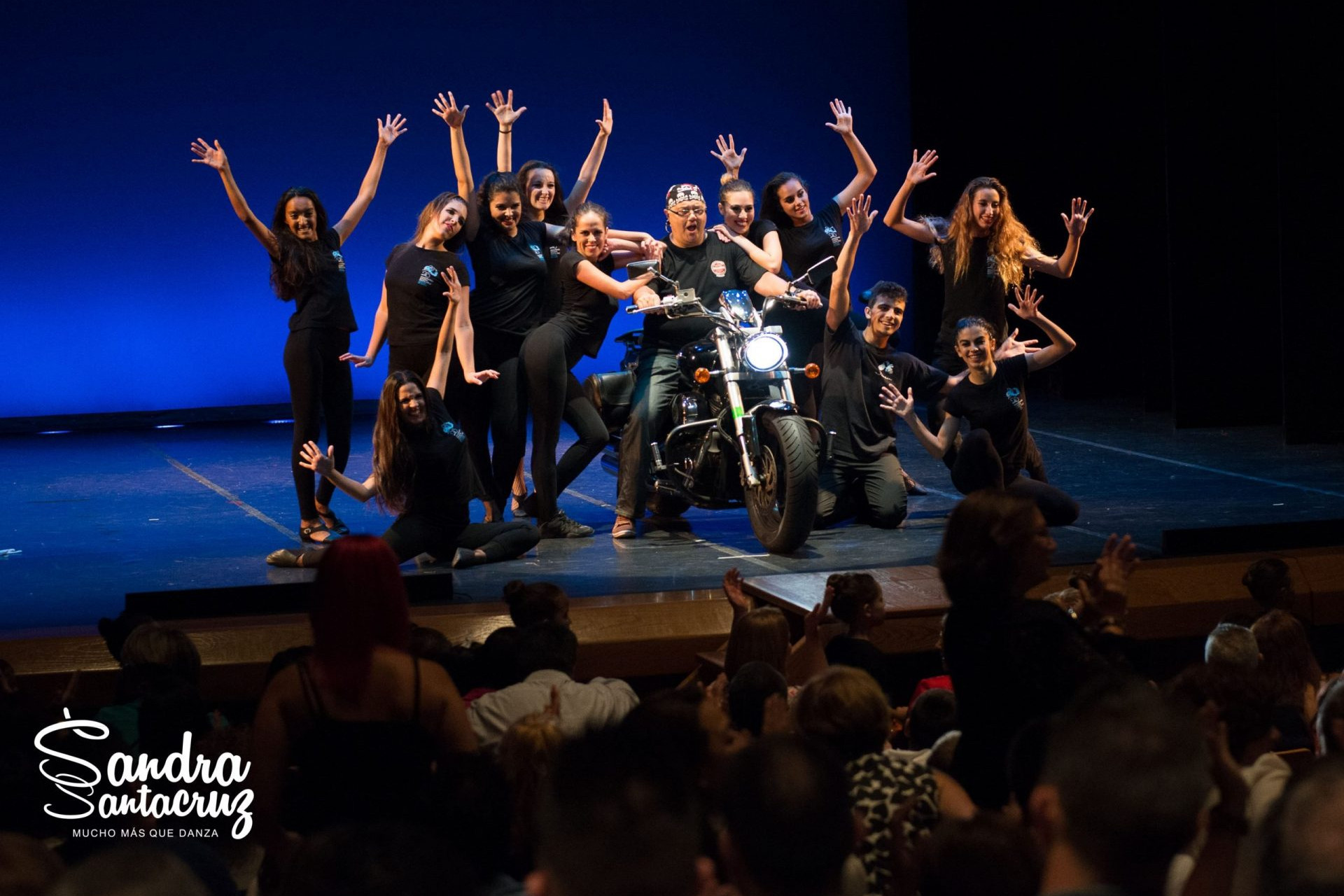 Foto de un espectáculo del Centor de Danza Sandra Santa Cruz con una motosobre le escenario y los bailarines bailan a su alrededor.