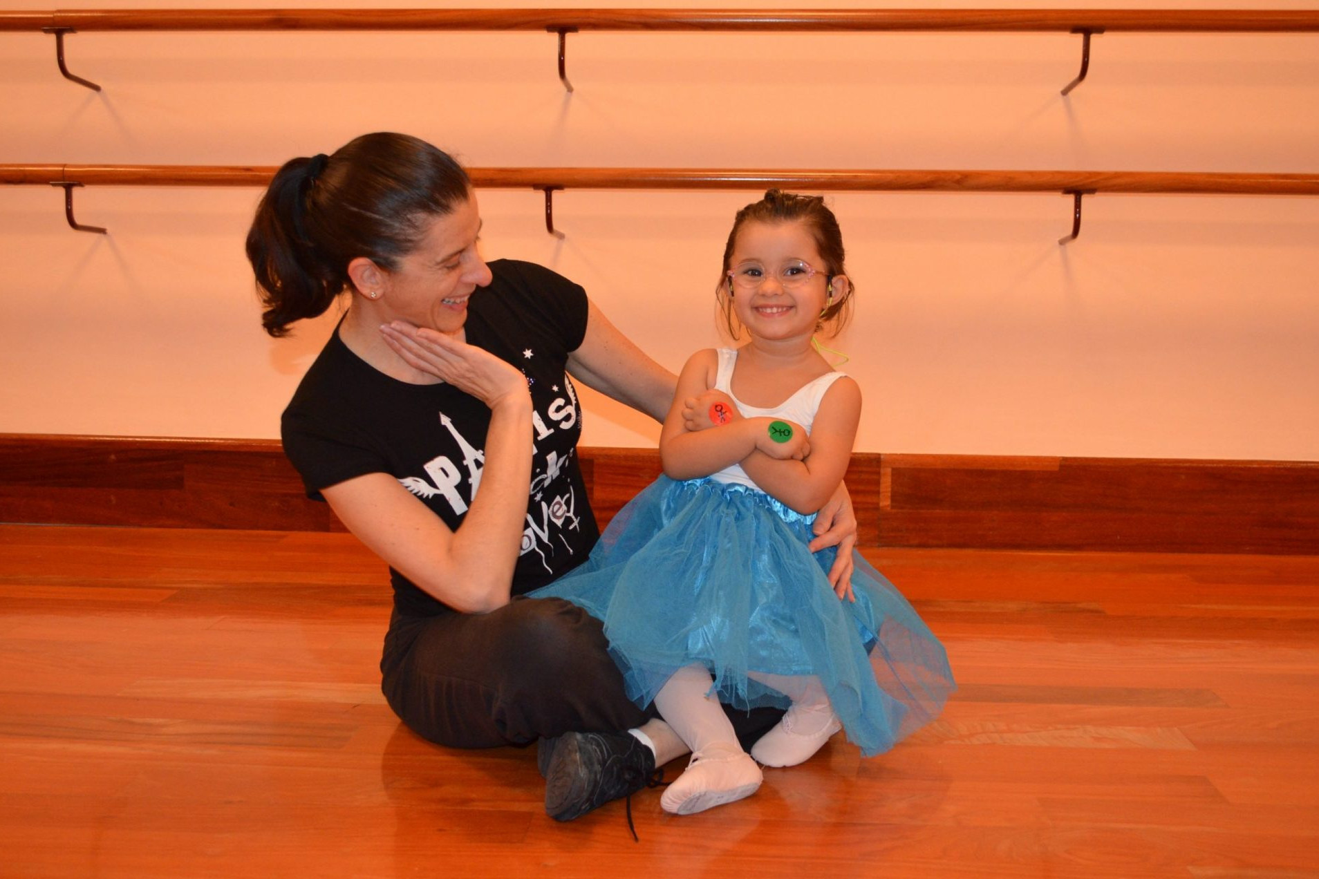 Foto en el Centro de Danza Sandra Santa Cruz en la sala de baile con Sandra y una alumna de predanza I de 3 años sentada en su falda en un ensayo para su estreno 