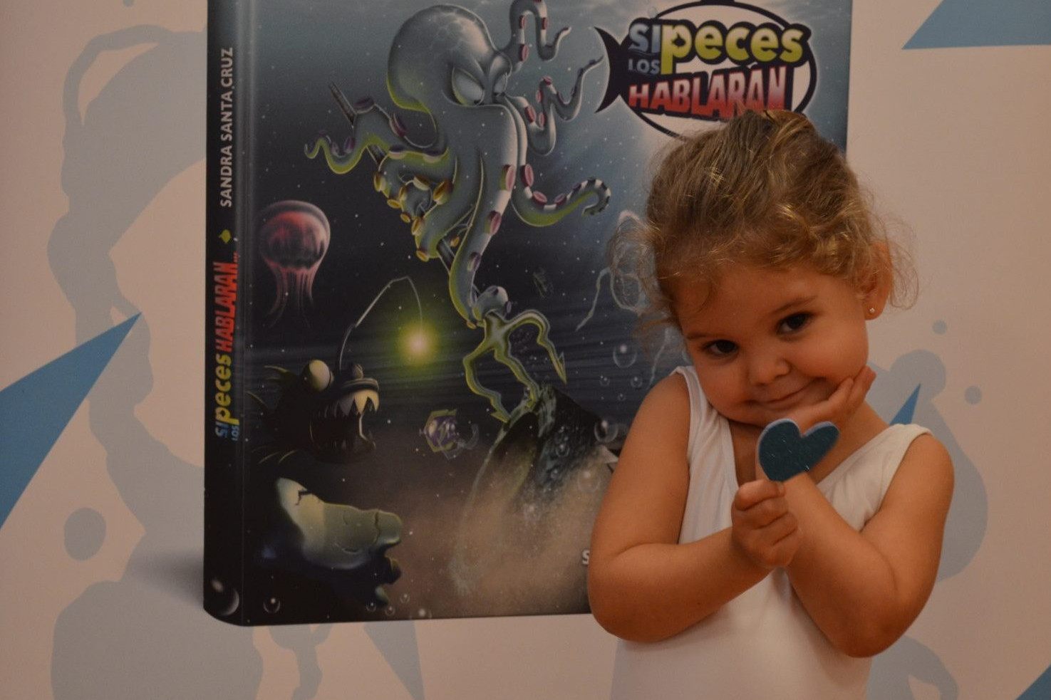 Intentando implicar a todos en el Día Mundial de los Océanos 2021_Foto de una alumna de 3 años del Centro de Danza Sandra Santa Cruz delante del photocall del cuento “Si los peces hablaran…” enseñando un corazón azul que tiene en las manos que simboliza el amor por la vida marina y que, por muy pequeño que seas, ¡tú también puedes cuidar el mar!