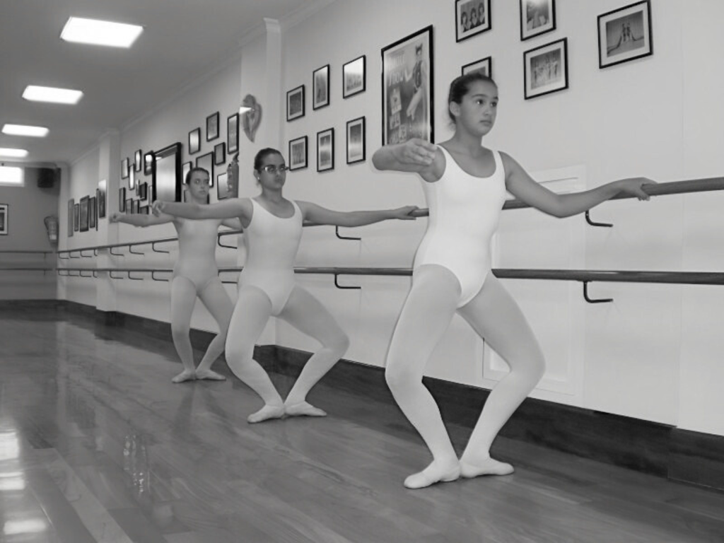 Tres bailarinas del Centro de Danza Sandra Santa Cruz haciendo un plié en primera posición en la barra.